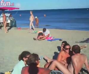 De geile huisvrouw pijpt de stijve lul van haar man op het naakt strand en trekt hem af, terwijl de mensen toe kijken.Pijpen en aftrekken op het naakt strand 